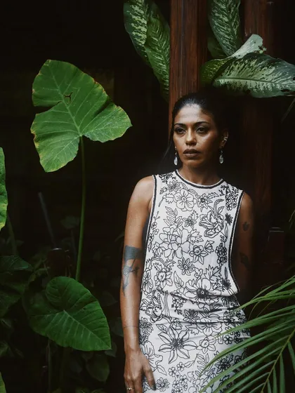 Anasuya Sengupta surrounded by large tropical leaves. The natural framing adds depth and a sense of place to the portrait.