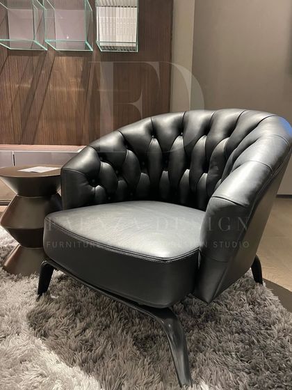 A luxurious armchair upholstered in black leather with classic button-tufting. Its enveloping shape and plush feel make it the perfect chair to sink into after a long day.