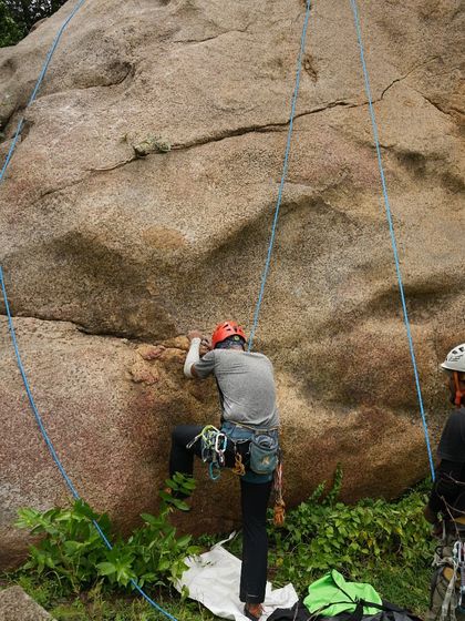 A climber starts up a route on a classic granite boulder, with a belayer ready below. This is a typical scene from our weekend group climbs.