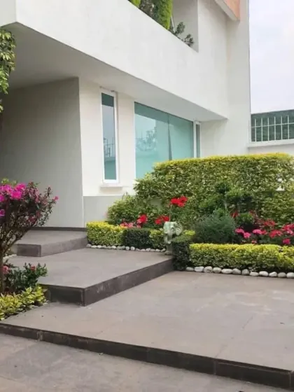 A formal entrance landscape featuring neatly clipped hedges, colorful flowering shrubs, and a clean, paved walkway. This style provides a structured and elegant welcome to the home.