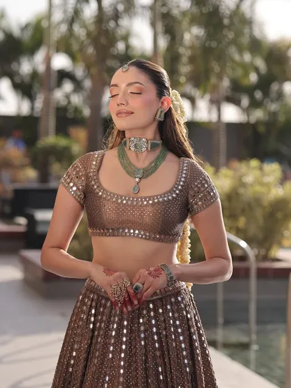 A serene moment captured. The bride's bronze lehenga and green jewelry create a beautiful contrast, showcasing a look that is both traditional and refreshingly modern.