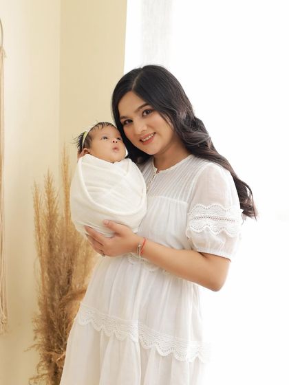 A beautiful mother smiling at the camera while holding her swaddled newborn. This is a classic portrait that captures the joy and pride of new motherhood.