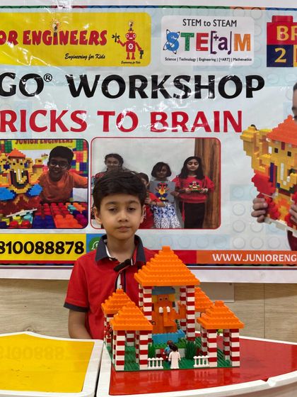 A boy stands in front of our workshop banner, showing off the red-roofed LEGO temple he built.