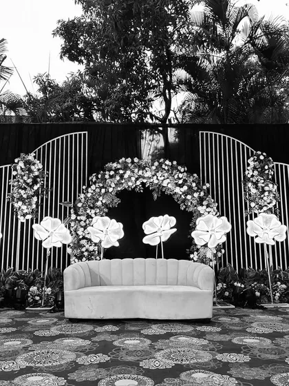 A black and white version of the stage, emphasizing the strong silhouettes and textures of the floral arch and illuminated flowers.