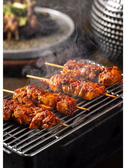 Sizzling chicken skewers on a tabletop grill, capturing steam and smoke for a dynamic effect.