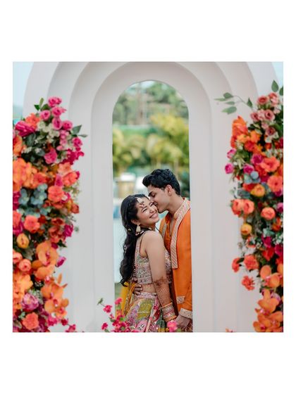 A sweet and romantic portrait of the couple framed by a floral archway. The groom's gentle kiss on her forehead is a perfect, tender moment.