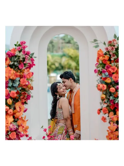 A sweet and romantic portrait of the couple framed by a floral archway. The groom's gentle kiss on her forehead is a perfect, tender moment.