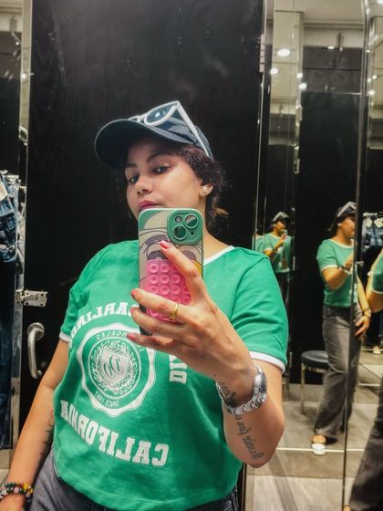 A quick selfie in the fitting room. The green graphic tee and cap create a sporty and casual vibe, perfect for a relaxed day at the mall.