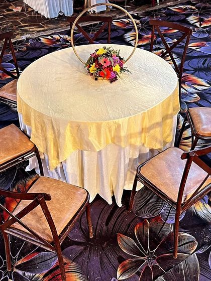 For a more rustic or classic feel, I offer wooden cross-back chairs. Here they are arranged around a simple round table with a cream-colored tablecloth and a floral centerpiece.