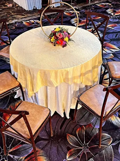 For a more rustic or classic feel, I offer wooden cross-back chairs. Here they are arranged around a simple round table with a cream-colored tablecloth and a floral centerpiece.