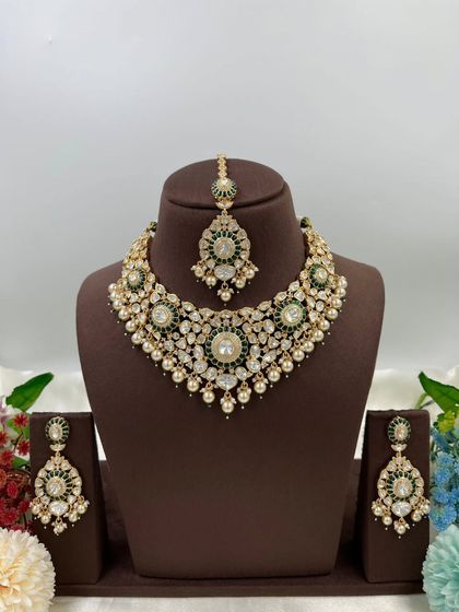 The Zarista Premium Moissanite Necklace set, shown here in both ruby and green variations. This set includes a necklace, maang tikka, and earrings, featuring large central stones surrounded by detailed craftsmanship.