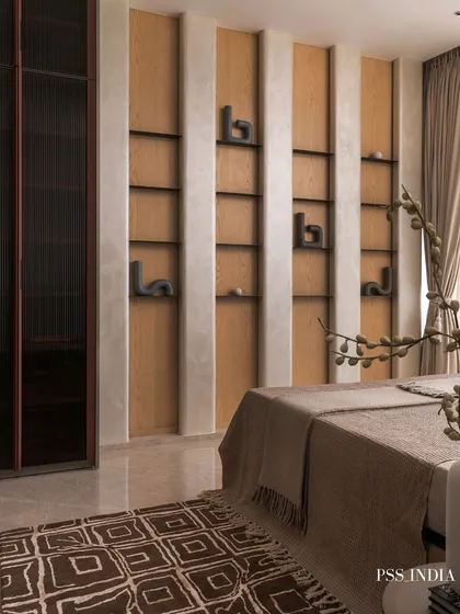 Built-in shelving with sculptural objects turns a simple wall into a curated display. The dark, fluted wardrobe and patterned rug add layers of texture and contrast to the space.