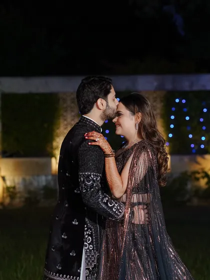 The couple shares a quiet, romantic moment during their sangeet. The groom's embrace from behind and their happy expressions create a heartwarming scene.