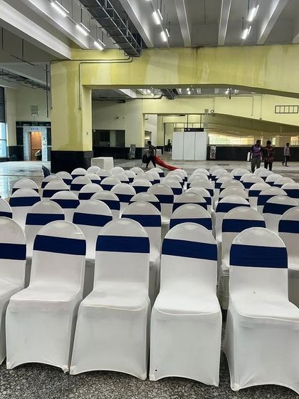 Rows of neatly arranged chairs with white covers and blue sashes. We provide large-scale seating solutions that are clean, uniform, and tailored to the event's color scheme.