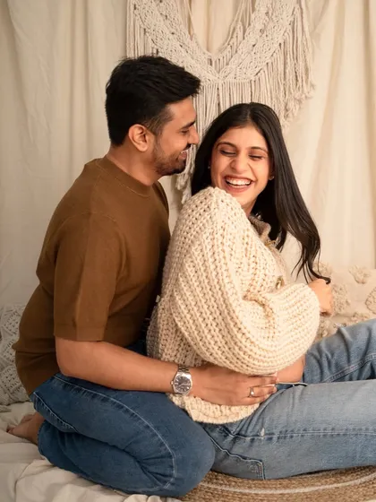 Capturing pure, unscripted joy. This candid photo shows a couple sharing a laugh during their cozy, casual maternity photoshoot in the studio.