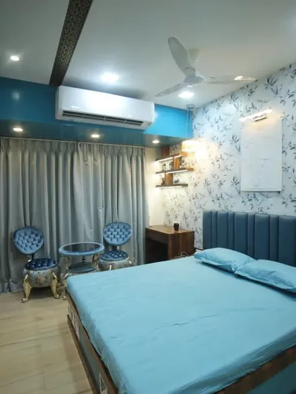 This master bedroom features a rich blue and wood theme. The design includes a custom upholstered headboard, elegant seating, and a feature wall with floral wallpaper for a classic touch.