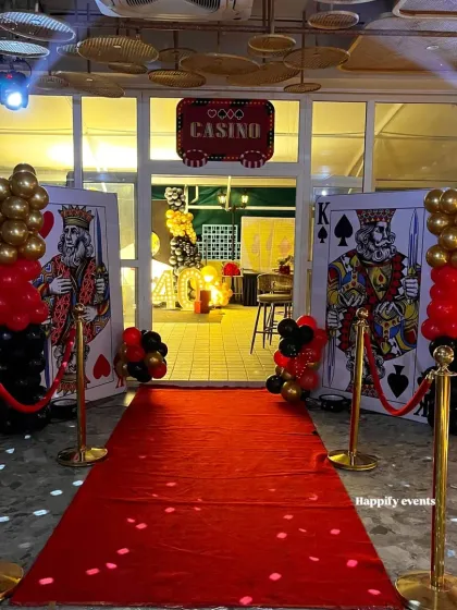Roll out the red carpet for an unforgettable celebration. This Casino Night themed party entrance features larger-than-life playing cards, a red carpet walkway, and gold stanchions, setting a glamorous and high-energy tone for an adult birthday or corporate event.
