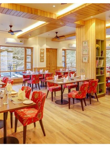 The resort's restaurant is filled with natural light and vibrant color. The chairs are upholstered in a custom fabric with patterns reminiscent of Himachali motifs, and the walls feature local artwork.