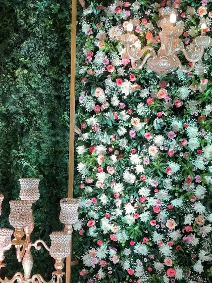 An enchanting photo corner combining a lush green wall with a dense wall of pastel roses and baby's breath. The elegant candelabra and crystal chandelier add a touch of modern romance, perfect for an engagement or reception.