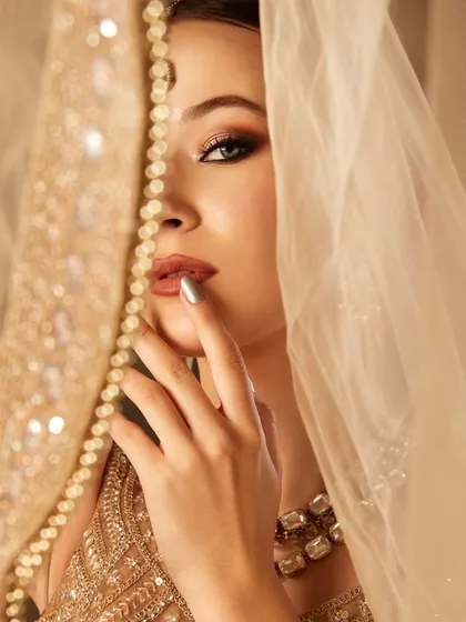 A soft and romantic shot of the bridal look, with the model peeking through a delicate, embroidered veil.