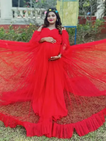 This vibrant red gown features a wide, ruffled trail and off-the-shoulder sleeves, offering a bold and glamorous look for an outdoor maternity shoot.