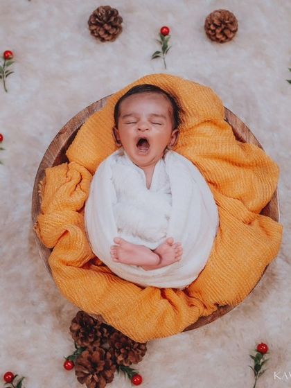 A sleepy yawn from a baby wrapped snugly in a wooden bowl. The festive props like pinecones and holly berries give this newborn photo a warm, winter-themed feel.