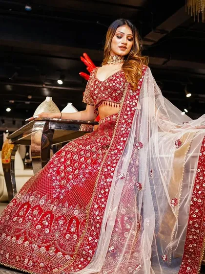 A full-length shot showcasing a magnificent red bridal lehenga by Study by Janak. The lighting is set to make the intricate embroidery and embellishments sparkle, presenting the outfit as a true work of art.