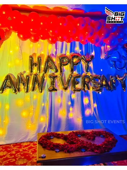 This popular anniversary decoration uses a backdrop of curtains and fairy lights, complemented by red balloons and gold foil 'Happy Anniversary' letters.