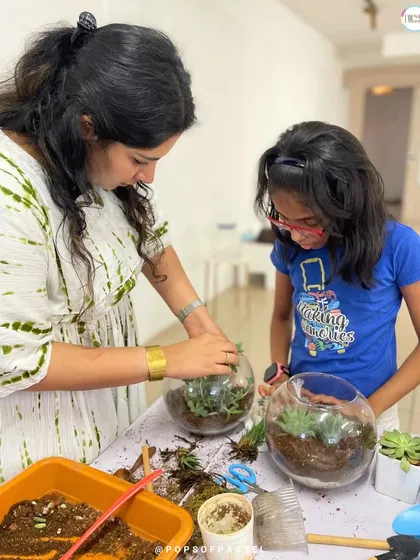 An instructor helps a young girl arrange the plants in her round glass bowl terrarium, teaching her about placement and care.