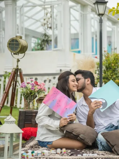 A creative and fun moment during a picnic where the couple gets artistic with paints. The groom gives the bride a sweet kiss on the cheek, capturing a candid and loving interaction.