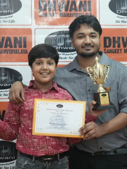 A student and his teacher with his two trophies, celebrating a successful year.