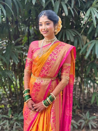 A portrait of the bride against a natural green background. Her makeup looks fresh and vibrant, complementing the colors of her saree.