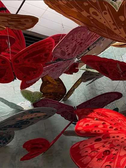 A close-up of the vibrant red butterflies from the 'We/Us' installation. The use of folded and shaped paper gives them a dynamic, fluttering quality.
