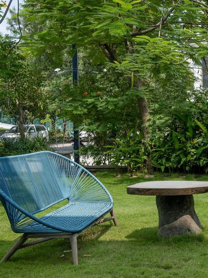 A modern blue bench and a rustic stone table create a simple, elegant seating area on a manicured lawn. This cozy corner is perfect for quiet contemplation, surrounded by mature trees that provide shade and serenity.