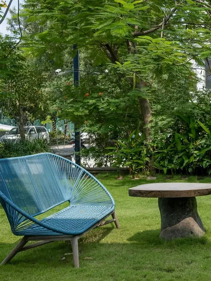 A modern blue bench and a rustic stone table create a simple, elegant seating area on a manicured lawn. This cozy corner is perfect for quiet contemplation, surrounded by mature trees that provide shade and serenity.