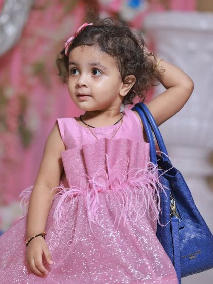 A little fashionista in the making! This portrait captures a girl in a sparkly pink dress, complete with a handbag, showing off her playful and stylish side.