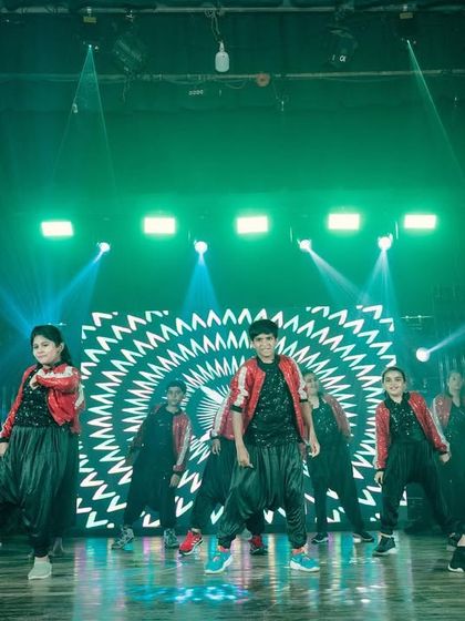 A hip-hop dance troupe performing on stage. The green beam lights and the hypnotic black and white pattern on the LED screen create a modern, edgy backdrop for their routine.