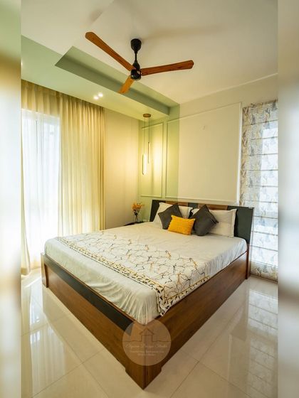 A guest bedroom with a calming pastel green accent wall and a false ceiling detail. The simple wooden bed and warm lighting create a serene and inviting atmosphere.