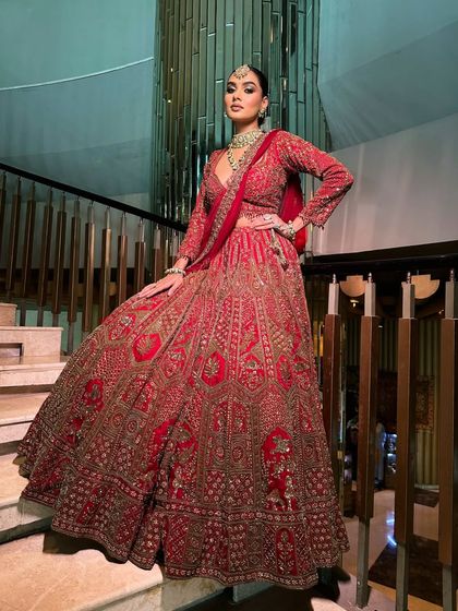 A full-length shot of the Tarz bride on a grand staircase, showcasing the magnificent flare of her red velvet lehenga.