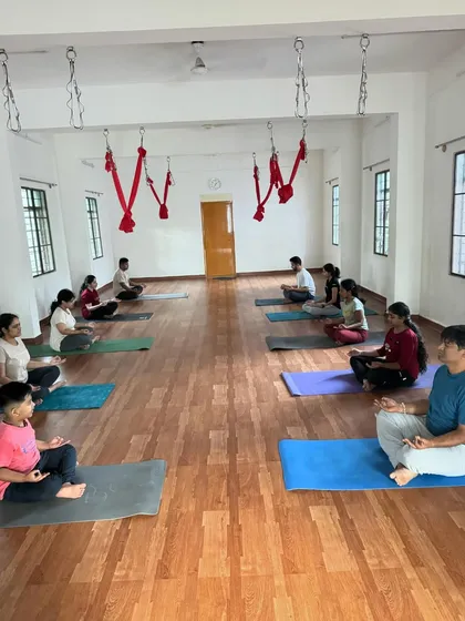 A moment of calm before our 6 am Yin Yoga session begins. Students are centered in Sukhasana (Easy Pose), preparing their minds for the practice ahead. The red hammocks for aerial yoga are visible in the background, showing the variety of classes we offer.