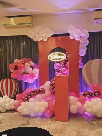 A vibrant hot air balloon welcome setup in shades of red and pink. The decoration features a large red arch, cloud-like balloon clusters, and hot air balloon props for a dreamy and exciting look.
