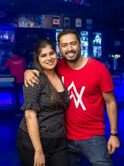 A smiling couple posing in front of the vibrant blue bar.