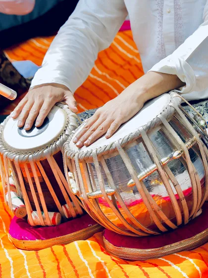 A close-up of my hands on the tabla, set against the bright colors of the stage.