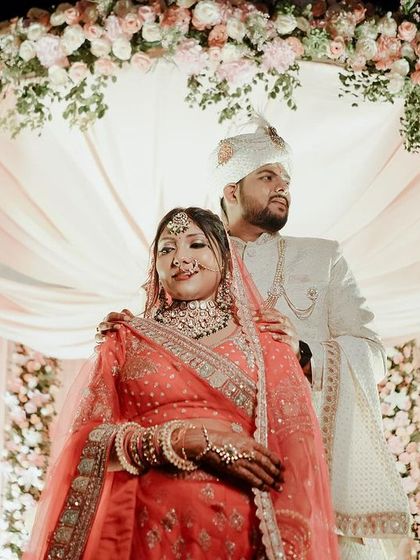 The couple posing under their beautiful floral mandap. The soft pink draping and the abundance of flowers create a romantic and picture-perfect setting.