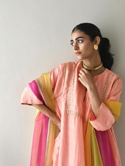 A model in a peach-colored kurta paired with a vibrant, multi-colored striped dupatta, a perfect look for a summer celebration.
