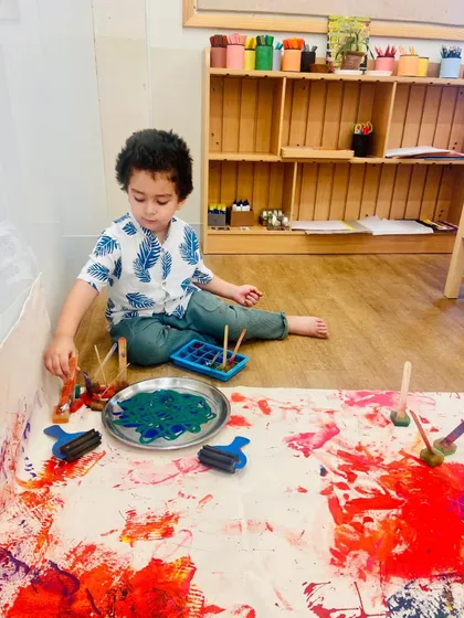 Seated on the floor, this child is immersed in his own world of process art. Using rollers and stamps, he explores how different tools create different effects, learning through experimentation and self-directed play.