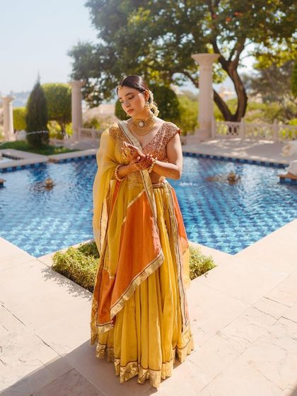 A full-length shot of Shree's custom Haldi outfit by the pool. The colors and silhouette are perfect for a daytime palace ceremony.