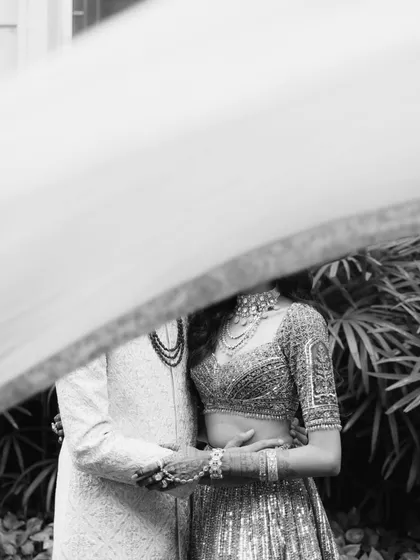 An artistic monochrome shot, with the couple partially obscured by a flowing veil. This creative composition adds a sense of mystery and focuses on the texture and detail of their wedding outfits.