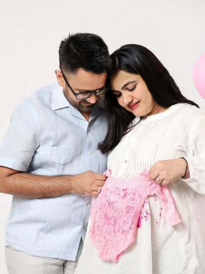 A tender moment as the couple looks at a tiny pink lace outfit for their baby girl. Using baby clothes as props makes the announcement feel so real.