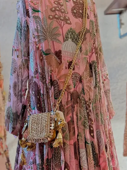 A detailed shot of the printed pink anarkali, featuring a charming forest and architectural motif, paired with a small, elegant handbag.